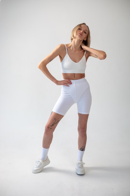 Foto ragazza bionda che posa su uno sfondo bianco in top e leggings