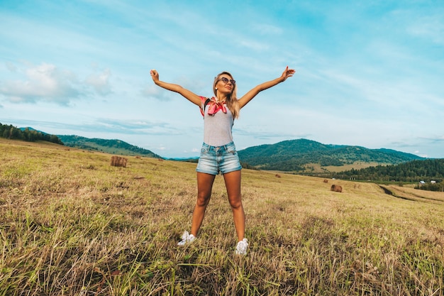 Blonde girl raised her hands up with a joyful emotion on her face. Young woman stretching up in a summer field.