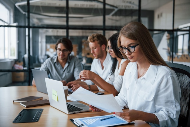 Blonde girl reads document. Young business people in formal clothes working in the office.