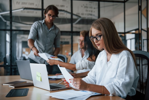 Blonde girl reads document. Young business people in formal clothes working in the office.