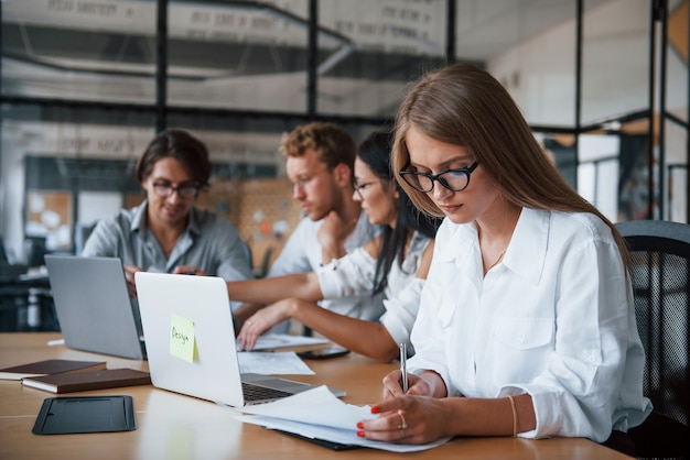 Blonde girl reads document. Young business people in formal clothes working in the office.