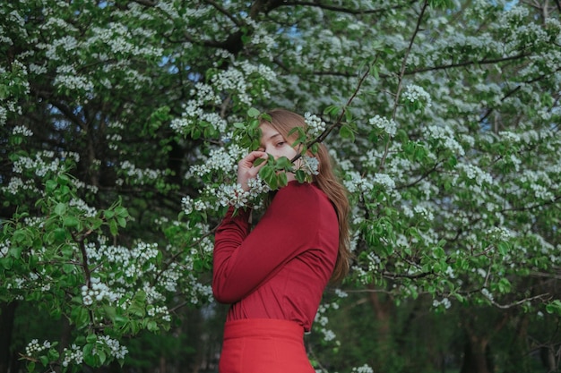 赤い服を着たブロンドの女の子が花の咲く木に隠れています