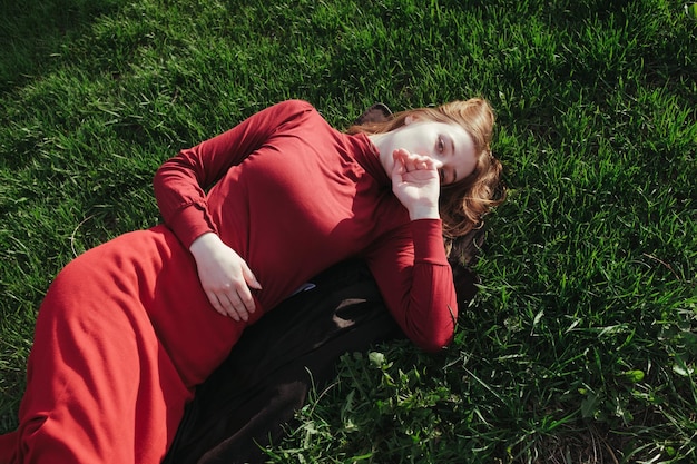 A blonde girl in red lies on the grass in the summer and enjoys the weather