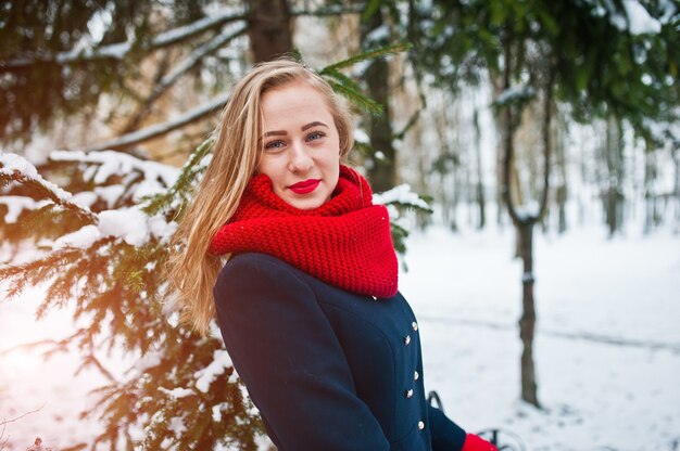 Blonde girl in red scarf and coat walking at park on winter day.