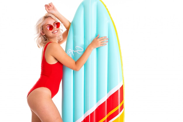 blonde girl in a red swimsuit and sunglasses with a swimming mattress