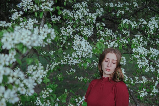 A blonde girl in red unites with nature in a garden of flowering trees