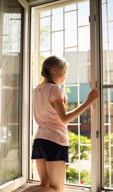 blonde girl sit on windowsill grid on window