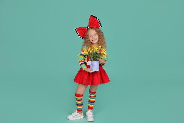 a blonde girl in a skirt knee socks and a Tshirt with a red bow holds a bucket of flowers