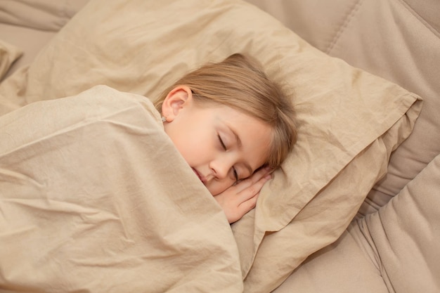 blonde girl sleeping in bed with a linen blanket