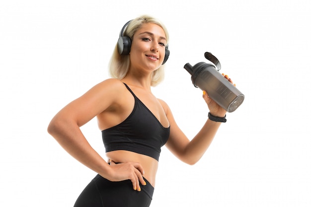 Ragazza bionda in uniforme sportiva tiene una bottiglia d'acqua e ascolta musica