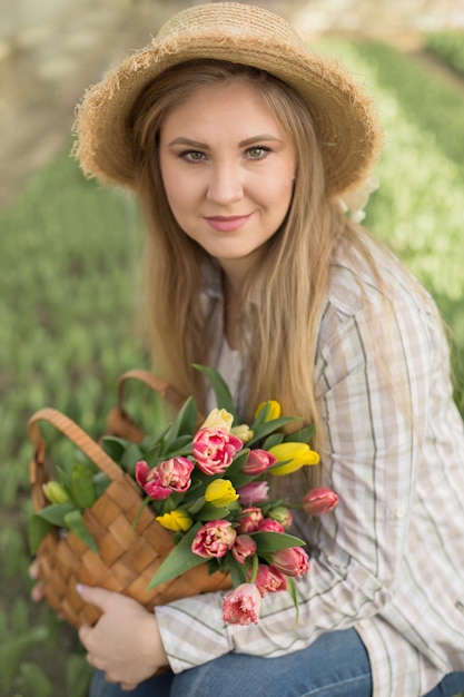 a blonde girl in a straw hat holds a straw bag with tulips in her hands