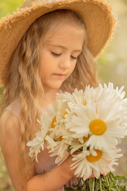 a blonde girl in a straw hat in a pink linen dress holds a bouquet of daisies in her hands