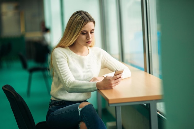 Blonde girl use phone in library