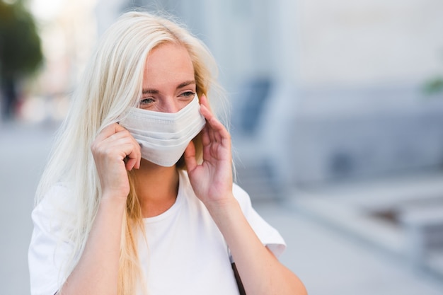 Blonde girl wearing medical protective mask walking in city street