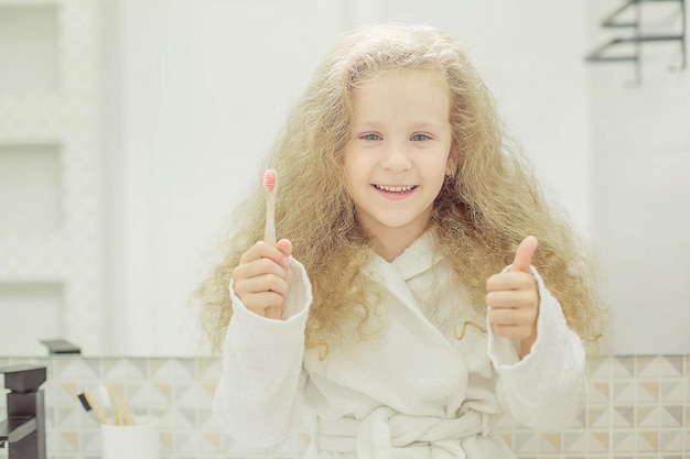 Una ragazza bionda in accappatoio bianco tiene in mano uno spazzolino da denti in bagno