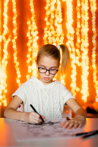 Blonde girl in the white knitting dress and big black glasses drawing santa claus. New Year theme