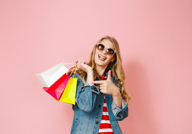 그녀가 한 쇼핑에 만족하고 분홍색 배경 위에 제스처를 보여주는 금발 소녀