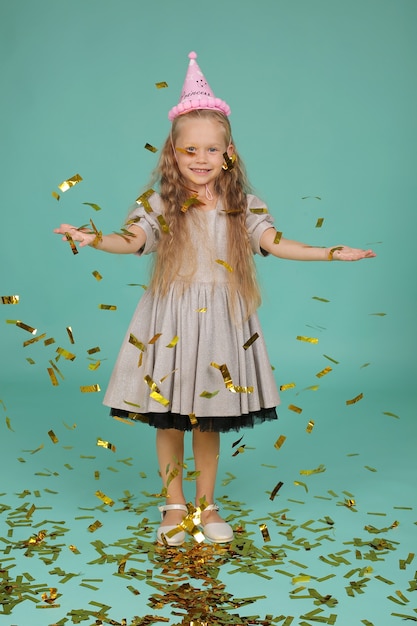 blonde girl with blue eyes in a gray dress in a hat happy birthday catches confetti