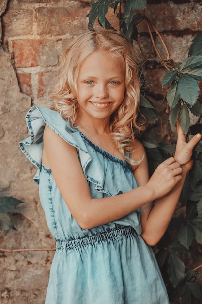 Blonde girl with curly hair posing against the wall with wild grape leaves. High quality photo