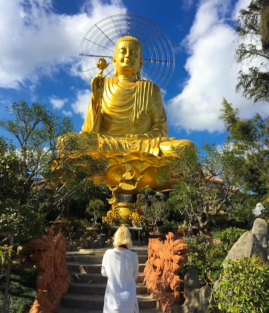 Блондинка с квадроциклом смотрит на золотую большую статую будды во вьетнаме, да лат, фотографии из t