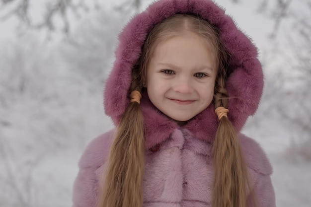 눈 덮인 겨울 공원에서 분홍색 모피 코트에 긴 머리를 가진 금발 소녀