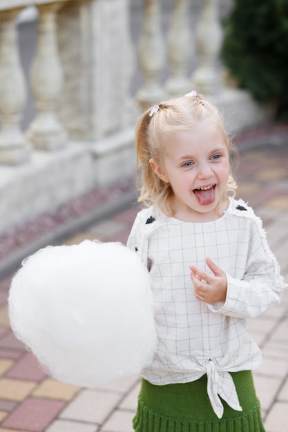 Blonde girl with sweet cotton wool in amusement park