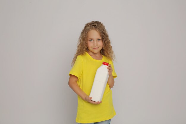 A blonde girl in a yellow tshirt with a plastic bottle of milk in her hands