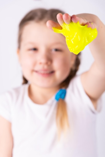 ブロンドの髪の子供は粘液で遊んでいます。小さな美しい白人の女の子が黄色いスライムで遊んでいます。スライムのおもちゃを再生する