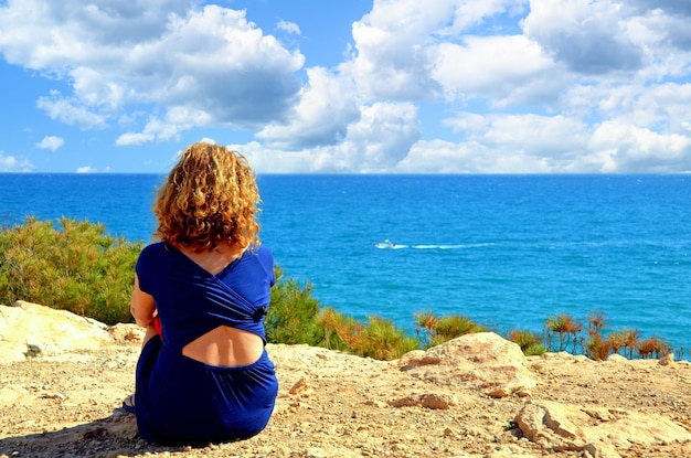 Blonde haired woman looking at the sea from the cliffs of torredembarra tarragona.