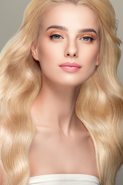 Blonde haren vrouw mooi krullend kapsel golvend lang haar natuurlijke make-up. Studio opname. op grijs