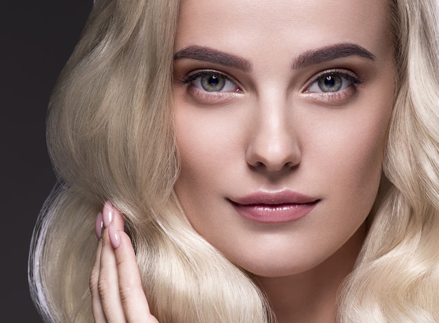 Blonde haren vrouw mooi krullend kapsel golvend lang haar natuurlijke make-up. Studio opname. op zwart