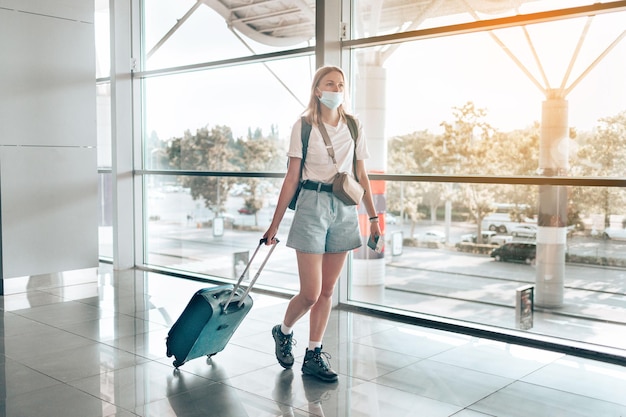 Blonde haren vrouwelijke toeristische hand met paspoort met koffer bagage wachtruimte van de luchthaventerminal voor een reis. Reizen na Covid-19 pandemie