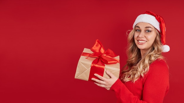 사진 그녀의 손에 선물 상자가 있는 산타 모자를 쓴 금발 빨간색 배경에 복사 공간이 있는 baner