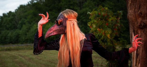 Blonde in kraaimasker poseert in de natuur in de buurt van oude boom