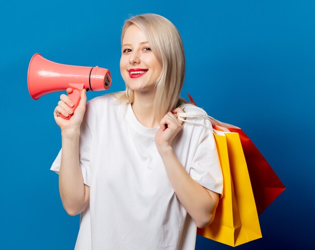 Blonde in wit t-shirt met megafoon en boodschappentassen op blauwe ruimte