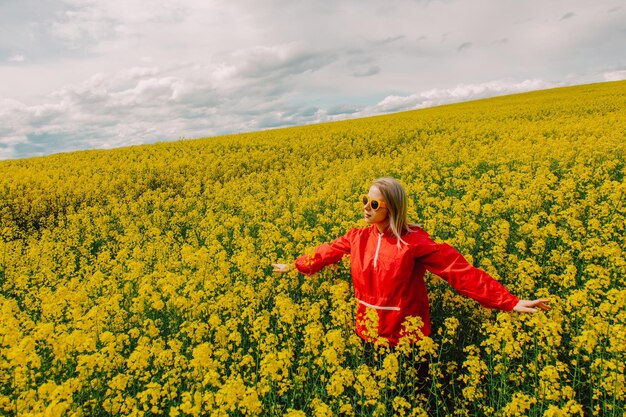 Blonde in zonnebril en rood trainingspak in koolzaadveld