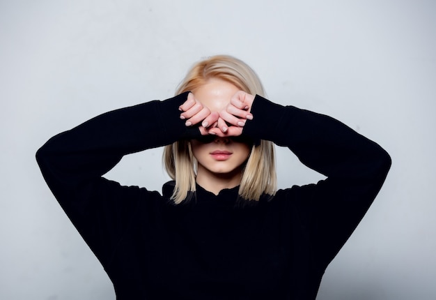 Blonde in zwarte hoodie verbergt een gezicht op een witte achtergrond