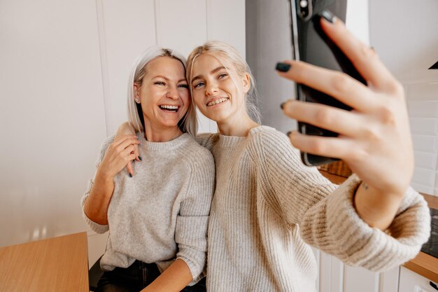 Blonde jonge gelukkige moeder en dochter in de keuken selfie maken voor sociaal netwerk en veel plezier bloggen familie blog