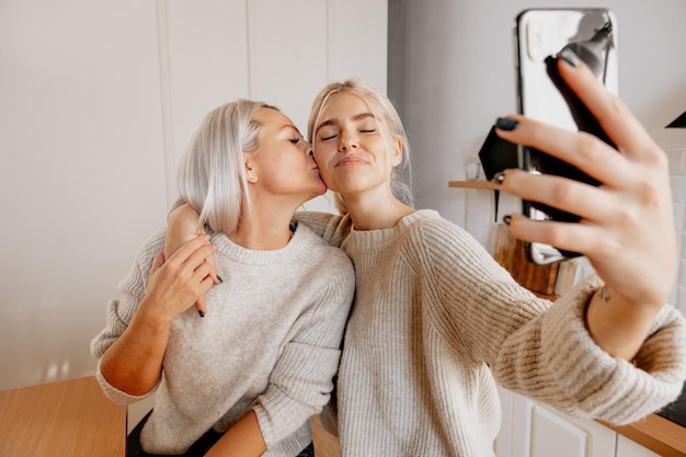 Blonde jonge gelukkige moeder en dochter in de keuken selfie maken voor sociale netwerk bloggering familie blog