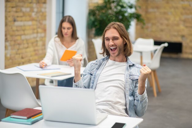 Blonde jonge man zit op de laptop en kijkt opgewonden