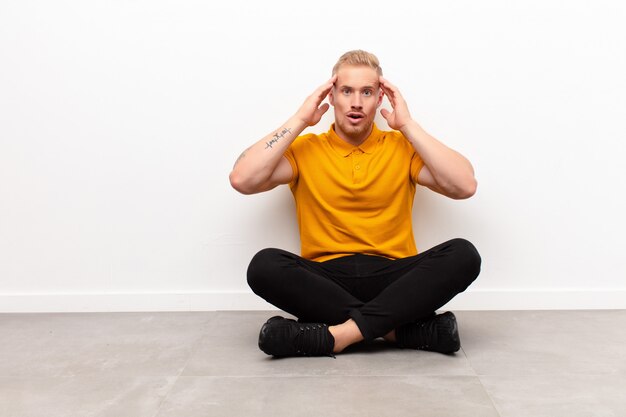 blonde jonge man zitten en gevoel geschokt