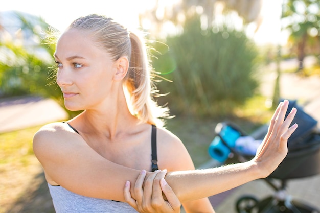 Blonde jonge moeder die buiten aan het trainen is om op te warmen met een yogamat op een tropisch strand