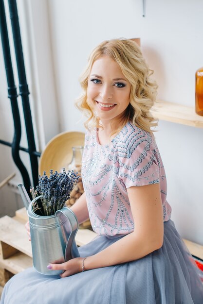 Blonde jonge vrouw die een bloem in een het planten balkonbinnenland houdt. Gezonde levensstijl, schoonheid, eco. Nul afval thuis concept