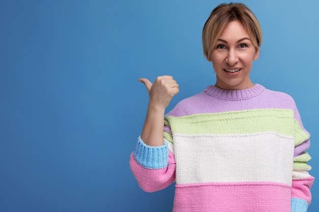 Blonde jonge vrouw in een fel jasje wijst met een vinger naar de ruimte van de muur op een blauwe achtergrond