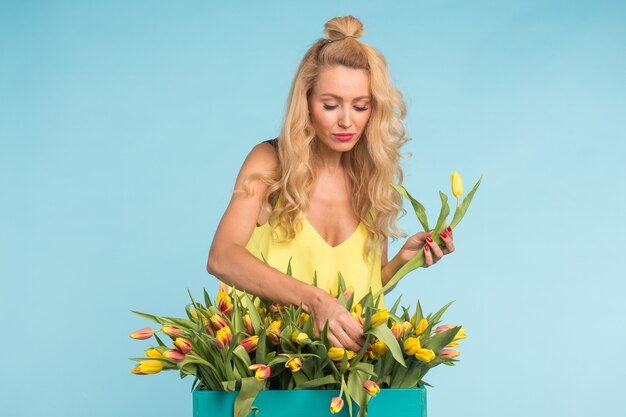 Blonde jonge vrouw met bos tulpen op blauwe muur