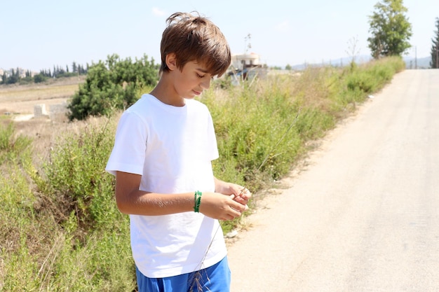 Foto blonde jongen in wit hemd en blauwe korte broek geniet van de zomerzon in de natuur