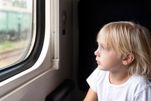 Blonde jongen kijkt bedachtzaam uit het treinraam. Treinreizen.