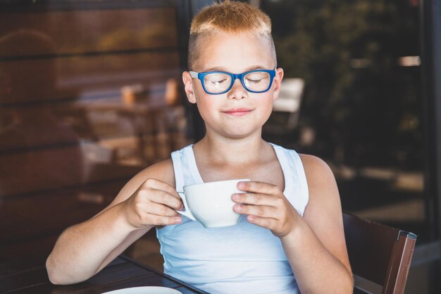 Blonde jongen met bril zit in een café en drinkt koffie