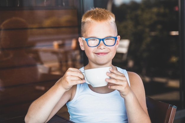 Blonde jongen met bril zit in een café en drinkt koffie