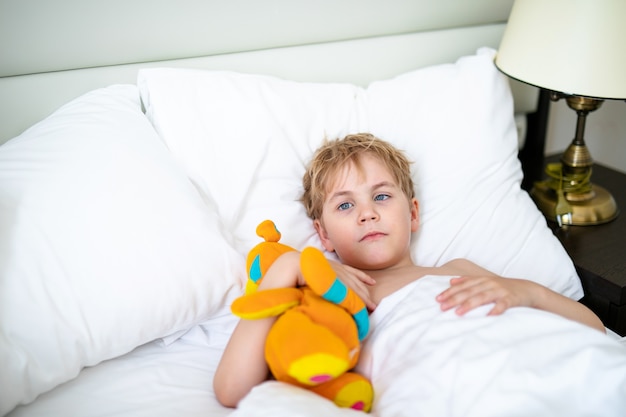 Blonde jongen met speelgoed oranje vos in het witte bed